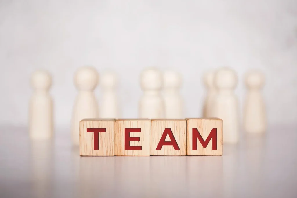 Aus Holzklötzen entsteht der Ausdruck „TEAM“ vor verschwommenen Holzfiguren.