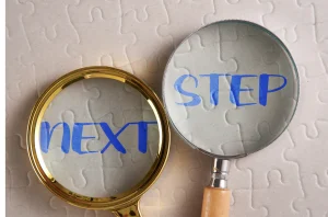 Zwei Lupen, die auf einem Puzzle platziert sind, mit den Worten "NEXT" und "STEP" unter jedem Glas.